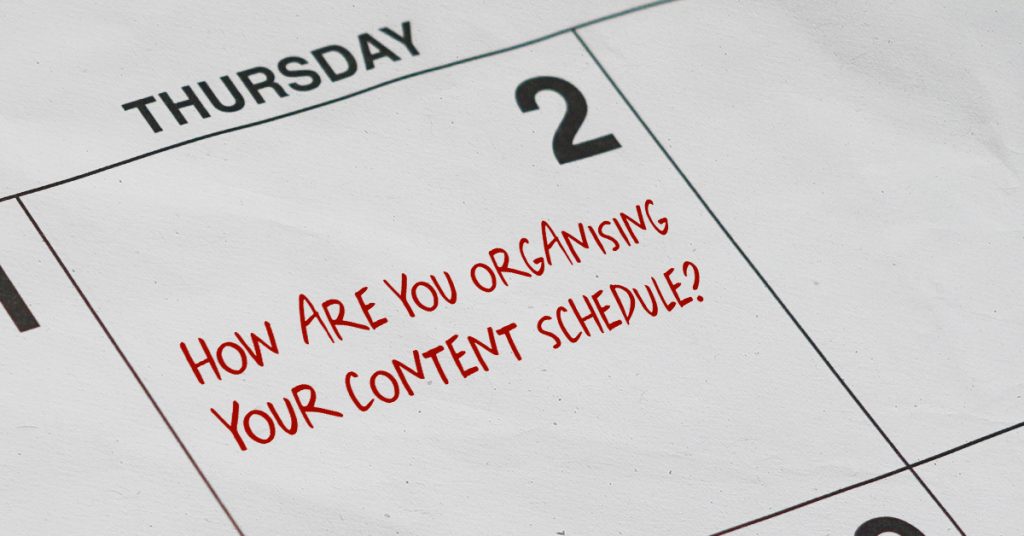 A calendar close-up featuring the day 'Thursday, 2' in bold black text. Written diagonally across the calendar page in red handwriting-style font is the question, 'How are you organising your content schedule?' The image suggests a focus on planning and time management.