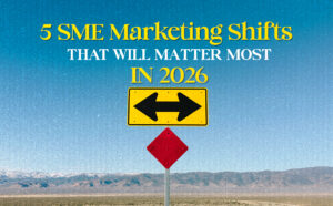 A road sign in a desert landscape with a blue sky shows two black arrows pointing in opposite directions on a yellow background, symbolising decision-making. Above it, bold text reads: "5 SME Marketing Shifts That Will Matter Most in 2026" in yellow and white serif font.